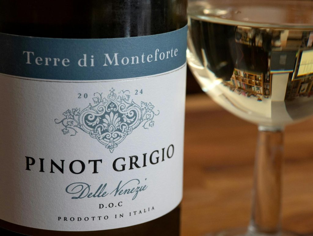 Fles Pinot Grigio wijn met etiket naast gevuld wijnglas op tafel