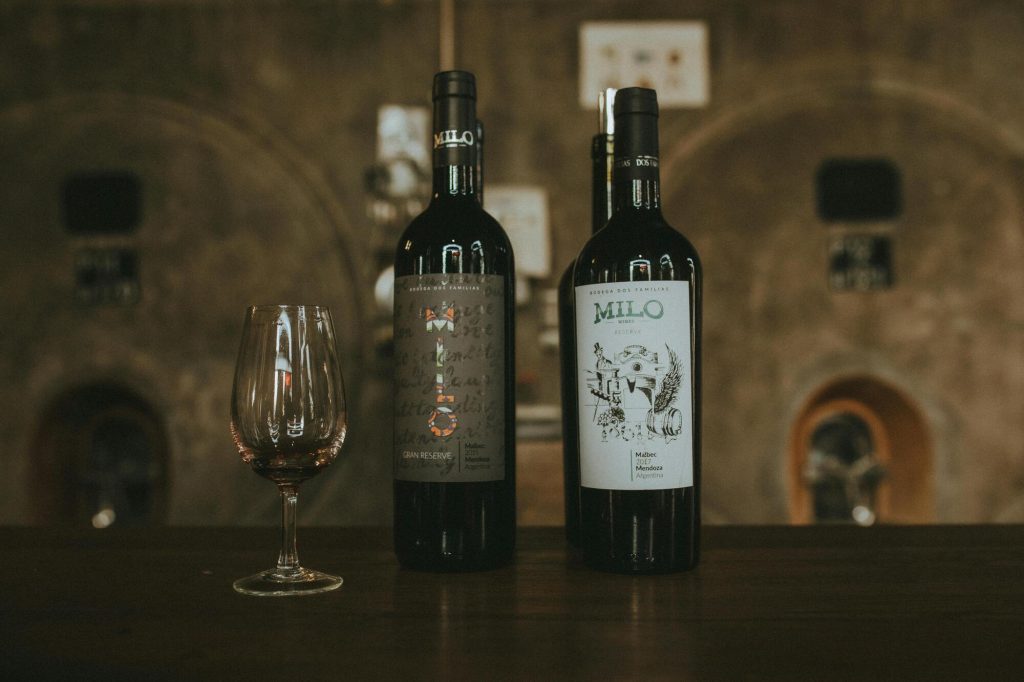 Twee flessen rode wijn en een leeg wijnglas staan op tafel in wijnkelderomgeving